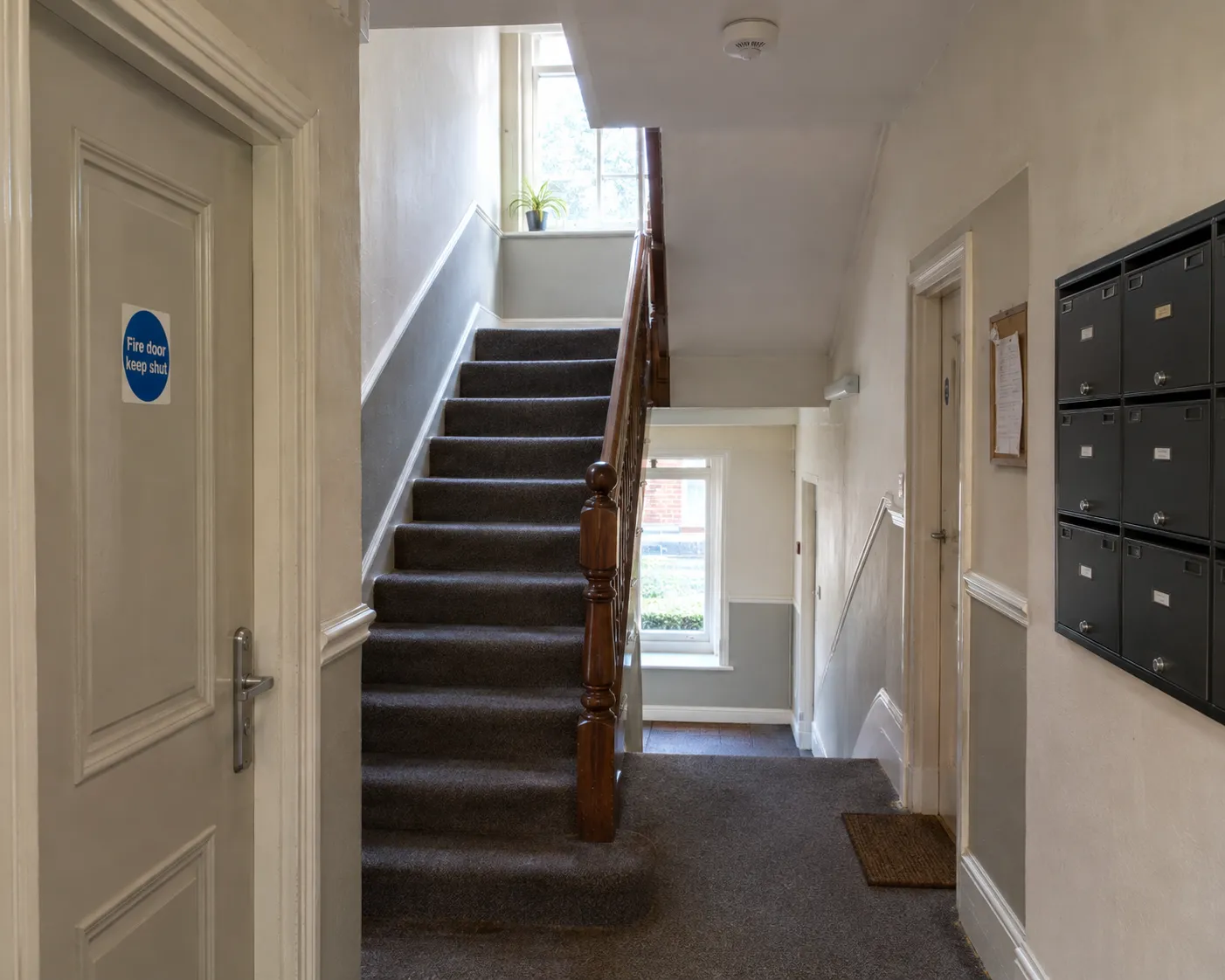 The communal hallway and staircase of a converted residential building with a fire door in view